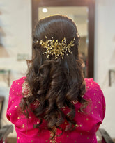 Woman with long, wavy hair wearing a gold hairpiece in a room.