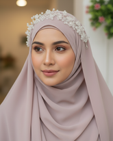 Woman wearing a light pink hijab with a decorative headband indoors.