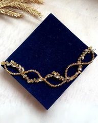 A hair vine named 'Mary Gold' featuring golden crystals and rhinestones in a twisted DNA shape, displayed on a blue velvet surface.