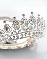 A close-up image of a silver bridal crown with sparkling rhinestones, showing the detailed design and the comb attached to the back.