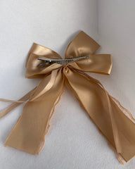 A beige hair bow with pleats and an alligator clip, adorned with a floral pattern at the center.