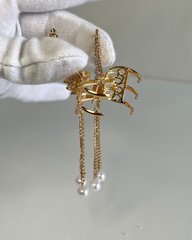 Gold earrings with intricate designs held by a gloved hand on a neutral background.