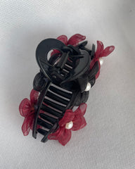 Black hair clip with red flowers and pearls on a light gray background
