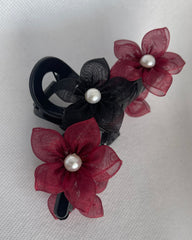 A black hair clip with fabric petals in black and red, featuring pearl detailing.