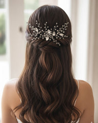 Woman with long, wavy hair wearing a decorative hairpiece in front of a blurred indoor background