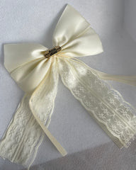 A black hair bow with pleats and an alligator clip, adorned with a floral pattern at the center.