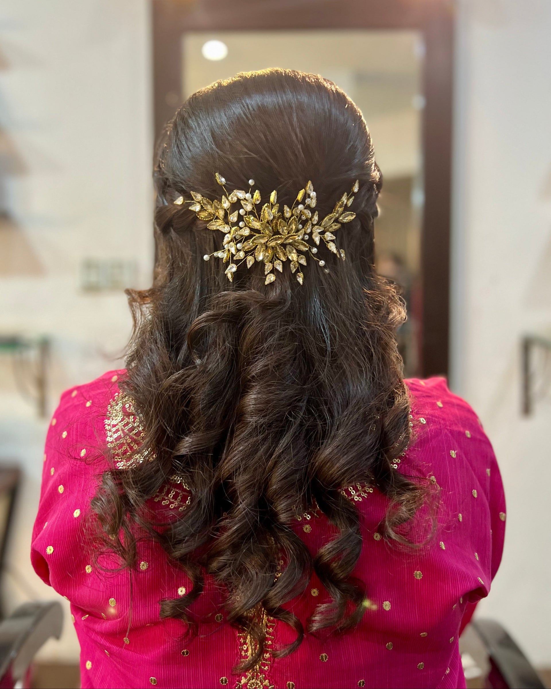 Woman with long, wavy hair wearing a gold hairpiece in a room.