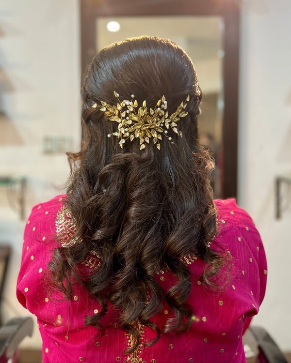 Woman with long, wavy hair wearing a gold hairpiece in a room.