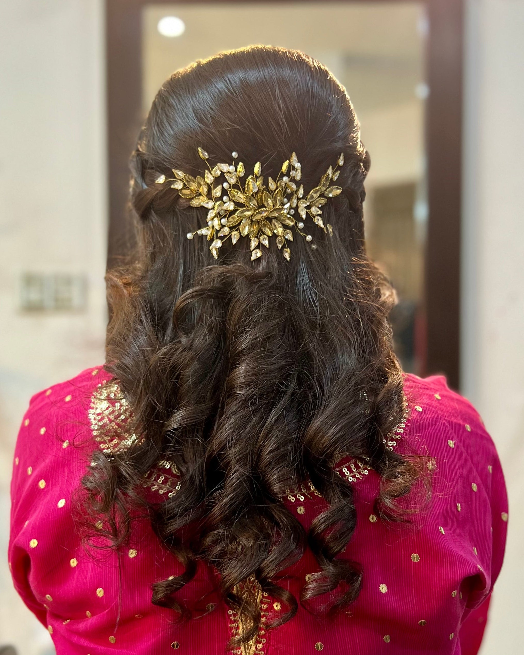 Person with long, wavy hair adorned with a decorative hairpiece, wearing a pink blouse.
