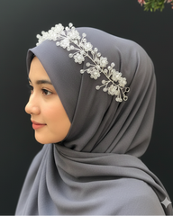 Woman wearing a gray hijab with a decorative headband against a dark background
