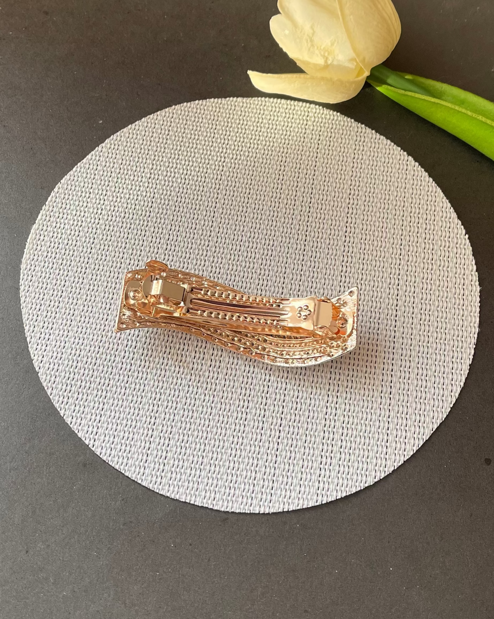 Rose gold hair clip on a gray surface with a white tulip in the background