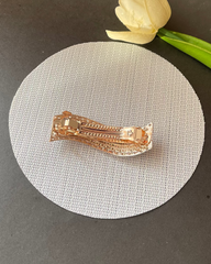Rose gold hair clip on a gray surface with a white tulip in the background
