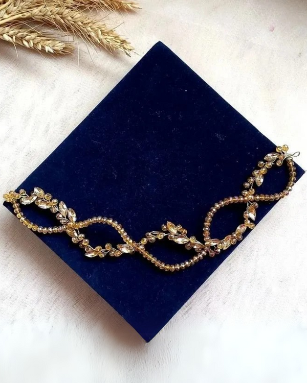 A hair vine named 'Mary Gold' featuring golden crystals and rhinestones in a twisted DNA shape, displayed on a blue velvet surface.