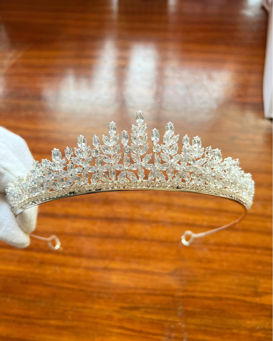 Silver tiara held by a gloved hand on a wooden surface