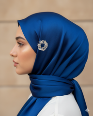 Woman wearing a blue hijab with a decorative brooch against a beige background